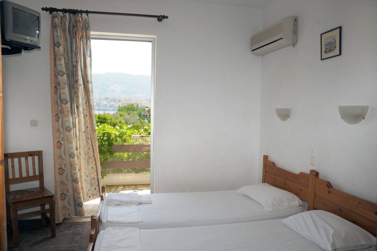 A bedroom with two beds, a chair, an air conditioning unit, and a view of greenery and mountains.