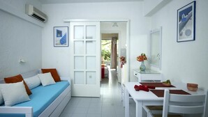 A bright, white room with a bed, a dining table, and a small kitchen area. - Ninetta's Studios (Poros)