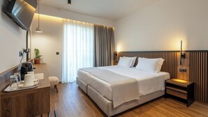 Une chambre d’hôtel moderne avec un grand lit, un bureau doté d’une machine à café et un téléviseur fixé au mur.