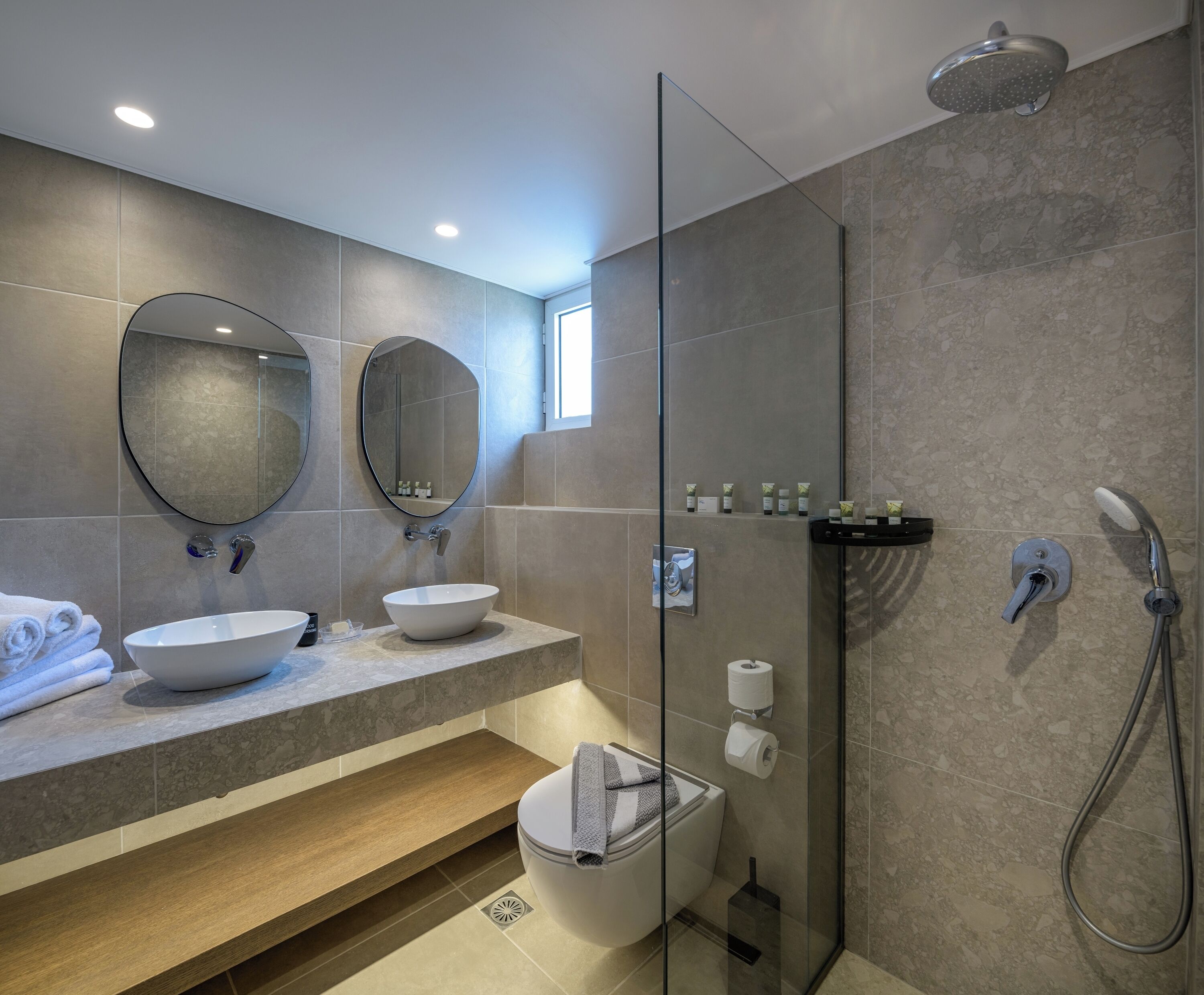 Un baño moderno con dos lavamanos, un espejo grande, cabina de ducha con paredes de vidrio y un inodoro.