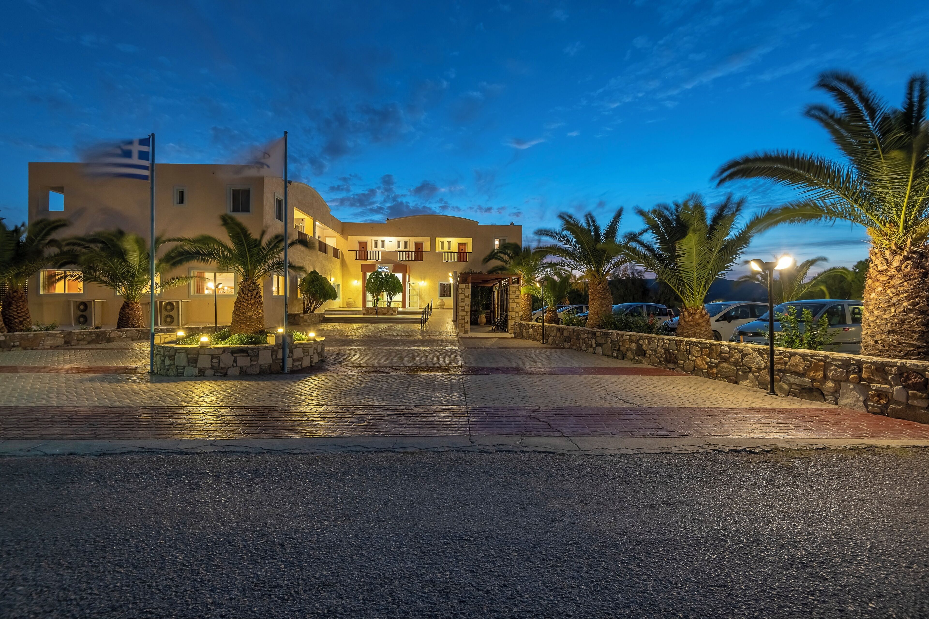 A hotel entrance with a paved driveway, palm trees, and a flag.