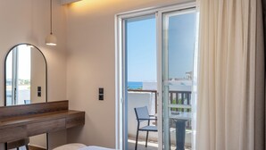 Une chambre moderne avec une table de chevet en bois, un grand miroir, un lit recouvert d’une couette blanche et une porte-fenêtre coulissante donnant sur un balcon équipé d’une table et d’une chaise.