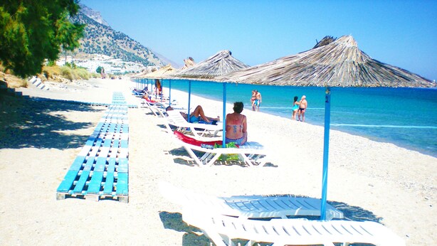 Une plage avec des transats et des parasols, un ciel dégagé et une montagne en arrière-plan.