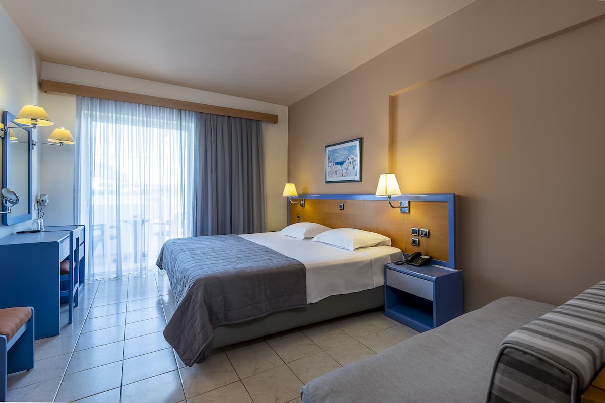 A hotel room with a bed, a desk, a chair, a nightstand, and a window with curtains.