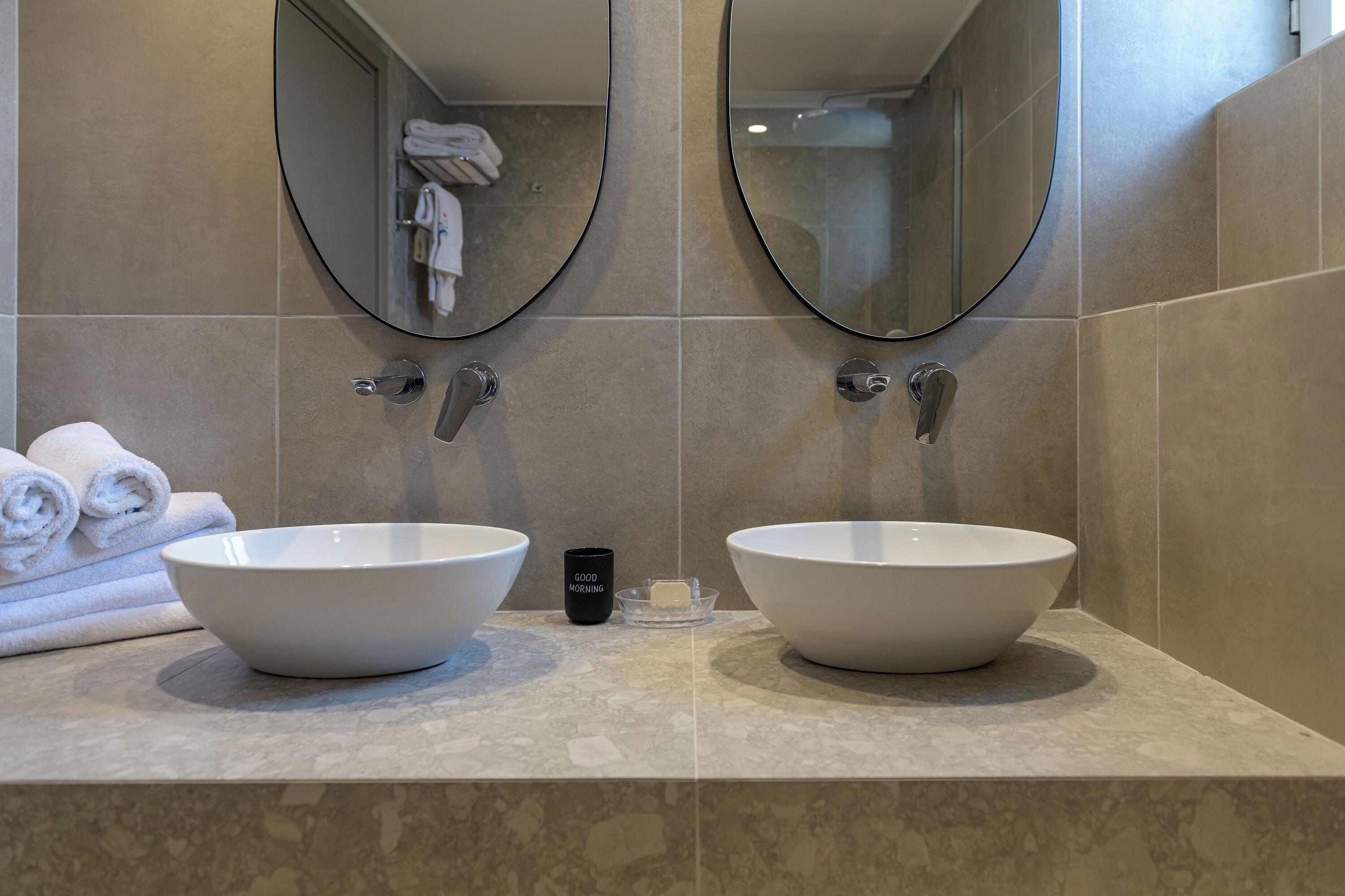 A bathroom with two large white sinks, a mirror above each, and a towel rack with folded towels.