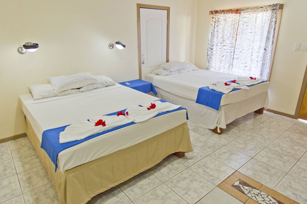 Dos camas individuales con ropa de cama azul y blanca, una puerta y una ventana con cortina estampada de flores.