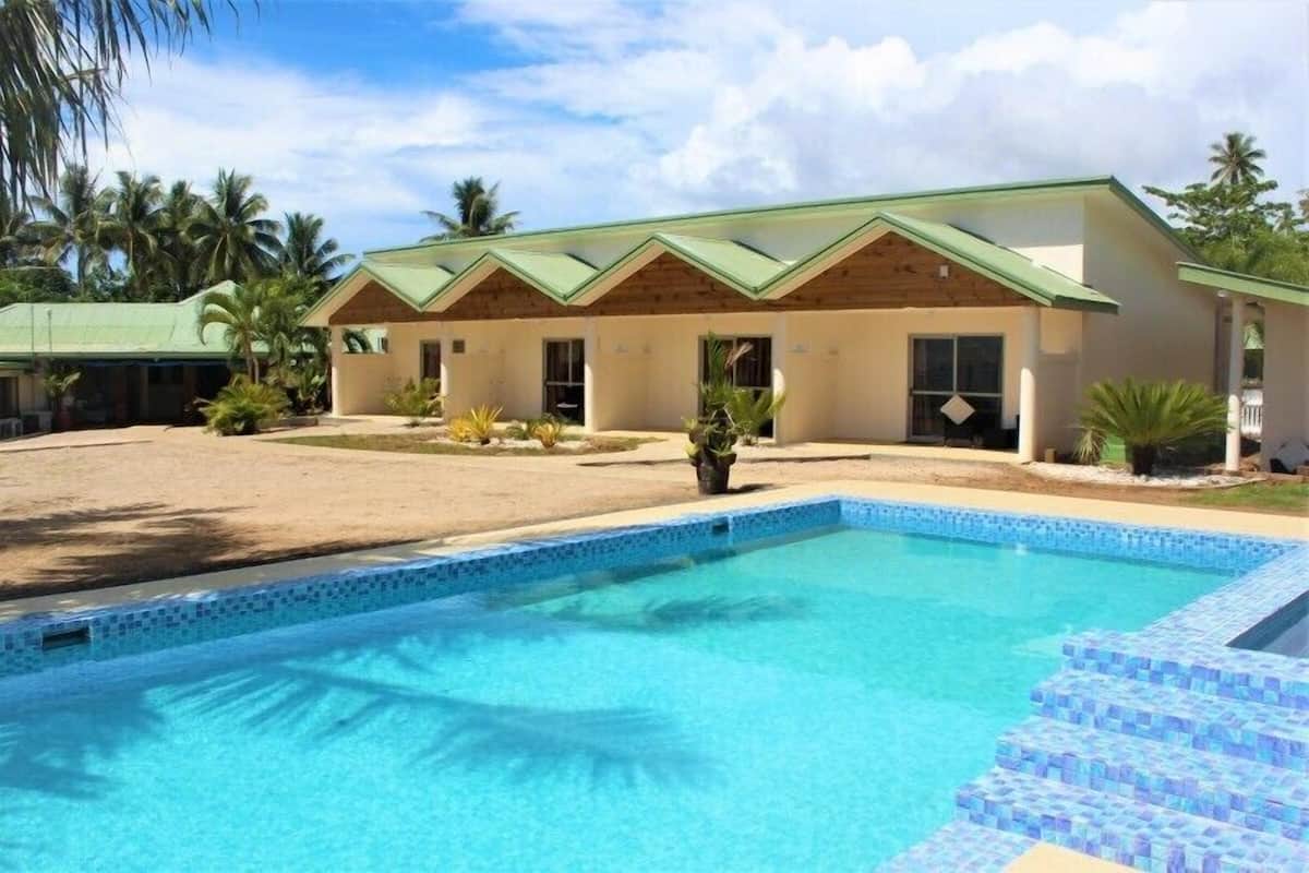 A hotel with a swimming pool, a covered outdoor area, and a building with a green roof.