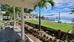 A covered outdoor area with a pool, palm trees, and a view of the ocean. - Le Uaina Beach Resort (Faleapuna)