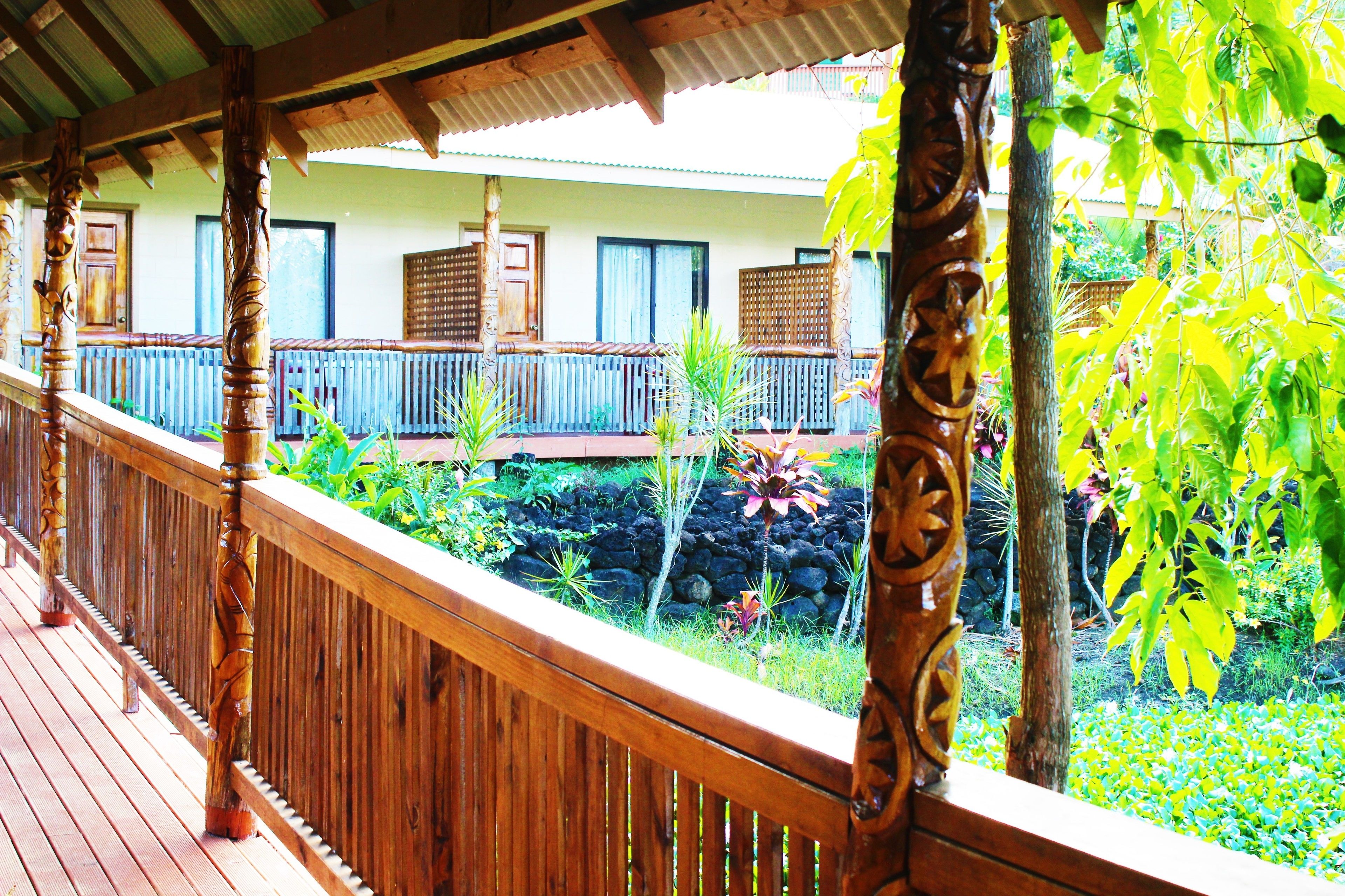 Une terrasse en bois avec une balustrade, un jardin de pierres et un bâtiment avec des fenêtres et une porte en arrière-plan.