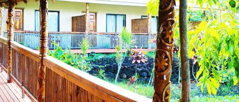 Une terrasse en bois avec une balustrade, un jardin de pierres et un bâtiment avec des fenêtres et une porte en arrière-plan.