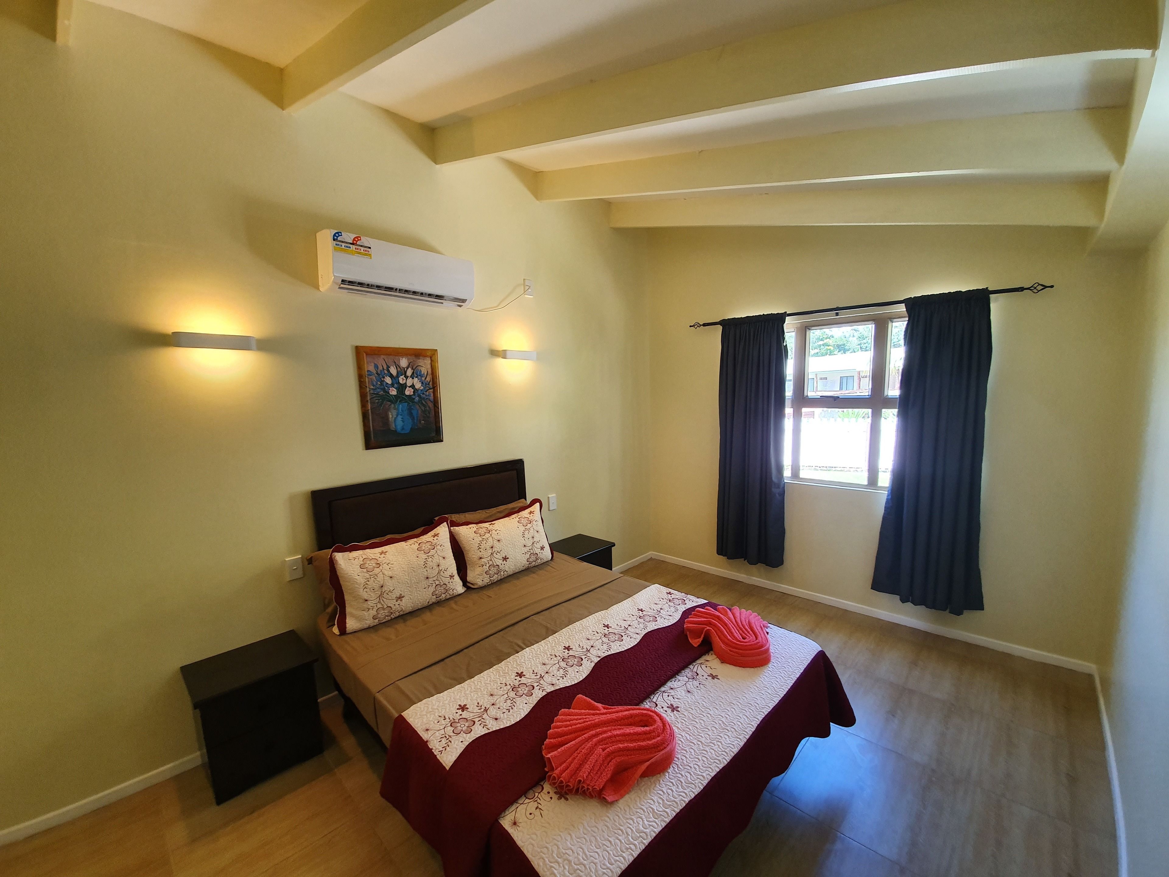 Een slaapkamer met een bed, een wandairconditioner, een schilderij en een raam met gordijnen.