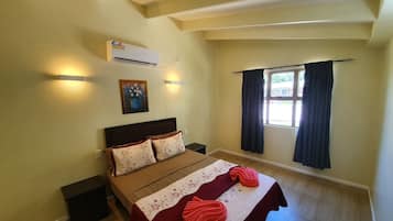 Een slaapkamer met een bed, een wandairconditioner, een schilderij en een raam met gordijnen.