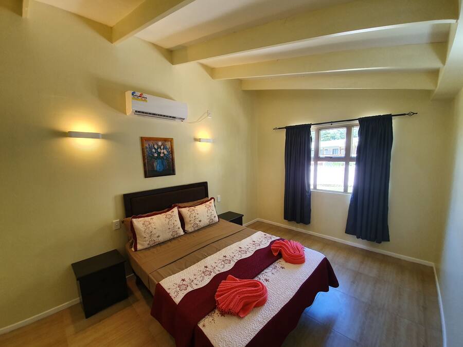 Een slaapkamer met een bed, een wandairconditioner, een schilderij en een raam met gordijnen.