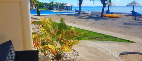 A pool area with a clear view of the ocean, palm trees, and beach chairs.