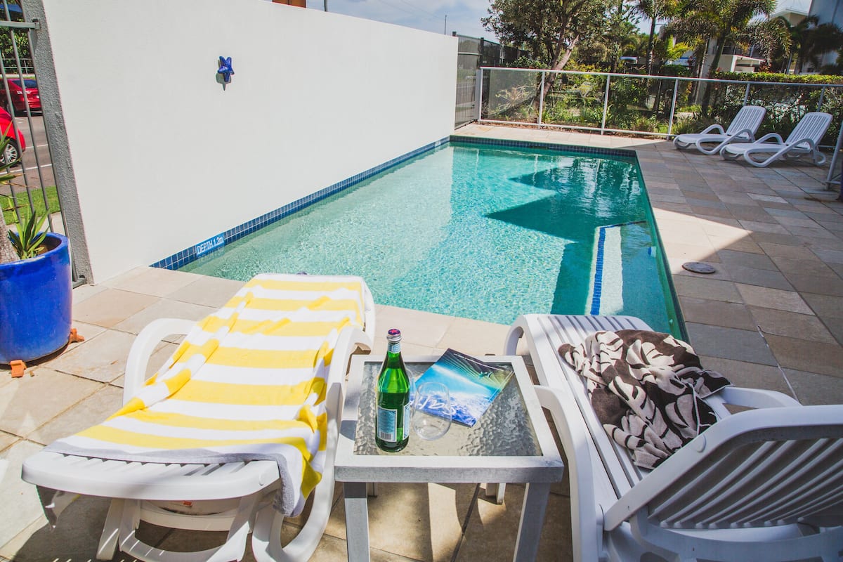 Piscina con sillones de descanso y una mesa con una botella y un vaso.