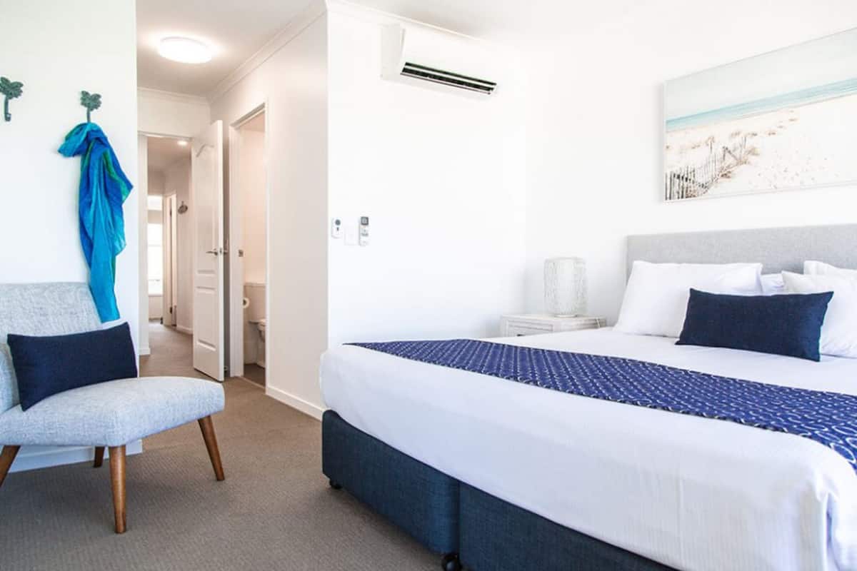 Habitación de hotel con una cama, una silla, aire acondicionado de pared y un cuadro.