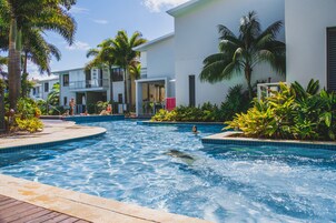 Zona de piscina con vista despejada, palmeras circundantes y un edificio con balcón.