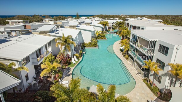Un resort con varias construcciones, una piscina central y vista al océano.