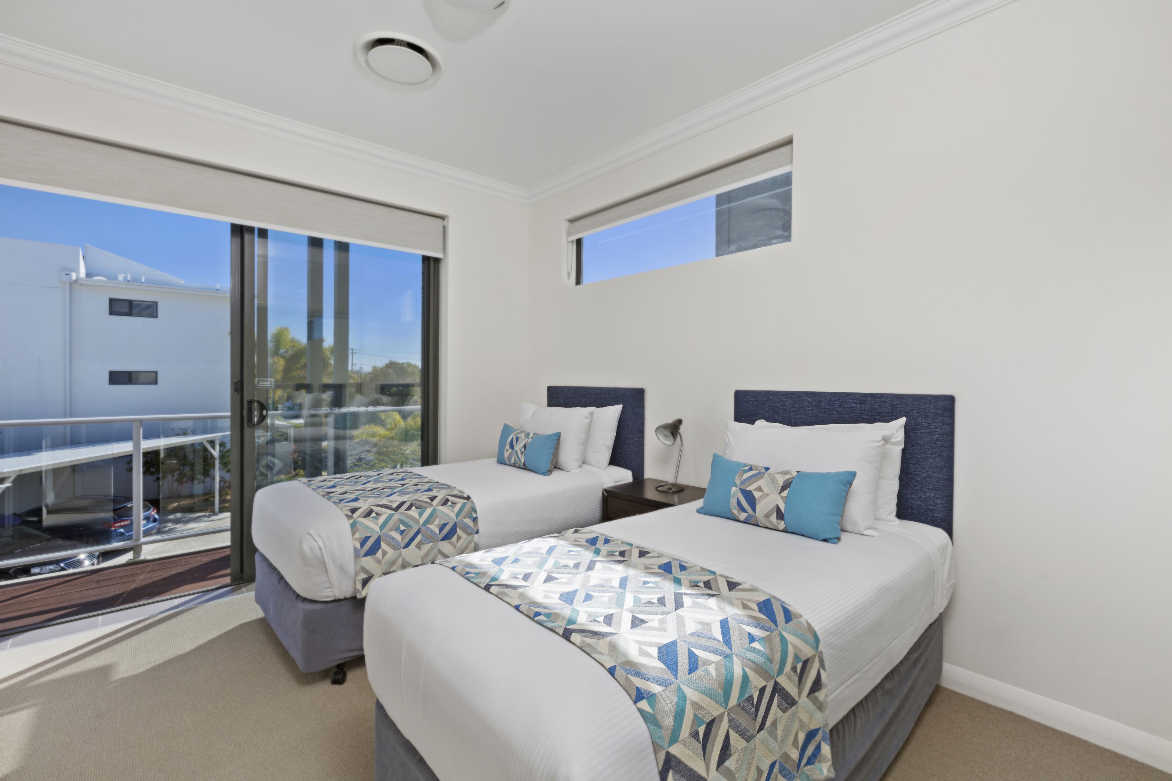 A hotel room with two beds, a balcony, and a view of the outside.