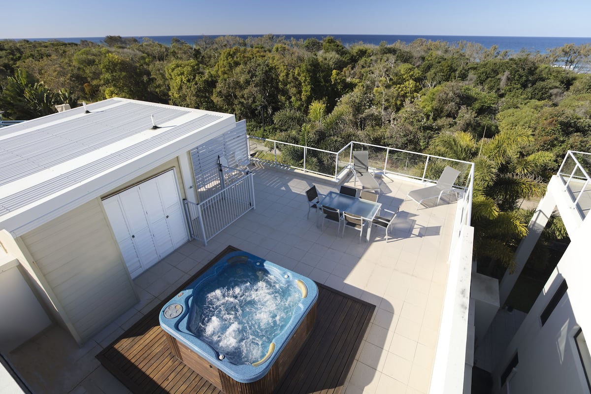 Un patio en la azotea con jacuzzi, mobiliario exterior y vistas al océano.
