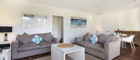 A modern living room with two grey sofas, a white coffee table, and a kitchen area in the background.