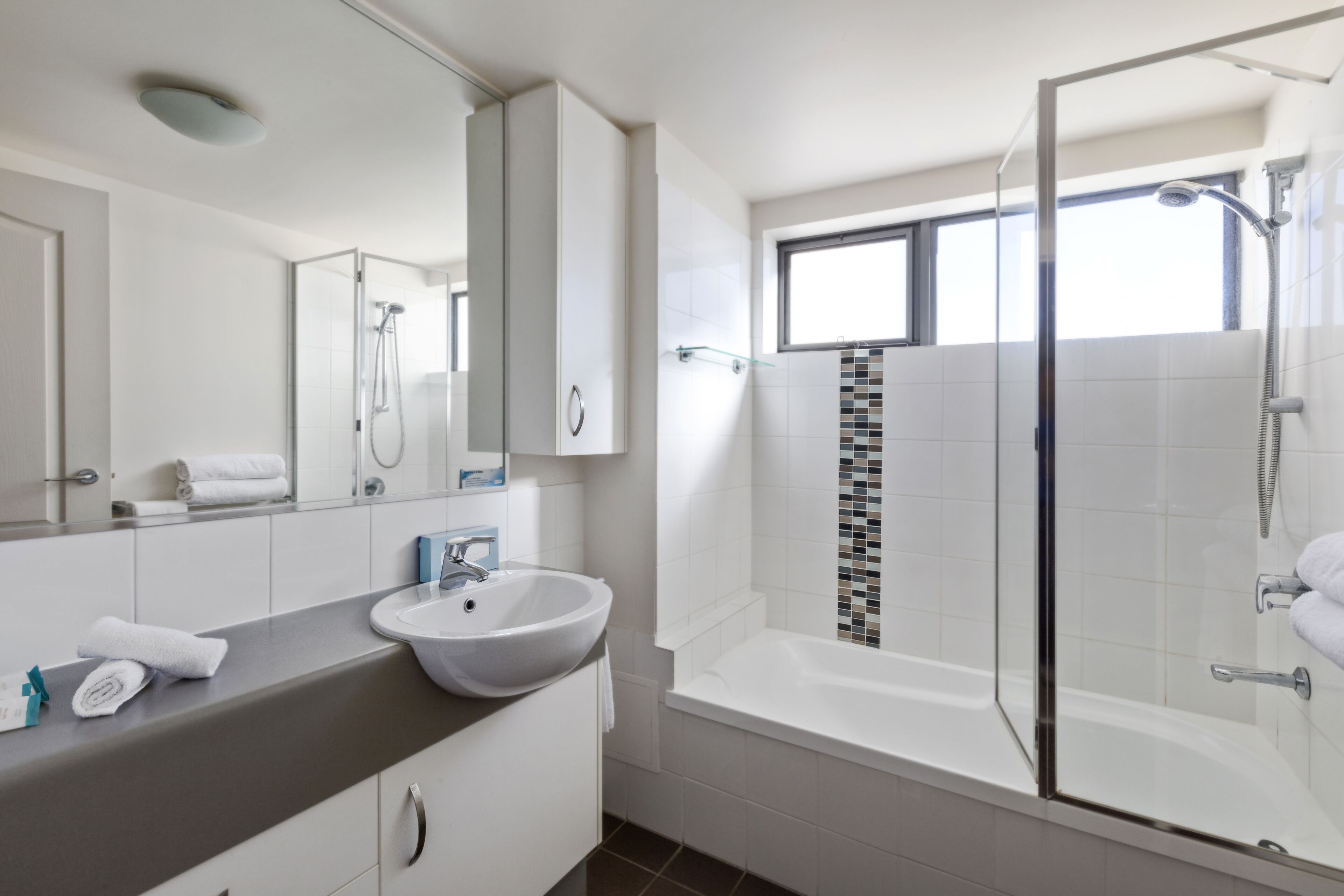 A modern bathroom with a glass-enclosed shower, a bathtub, and a large mirror above the sink.
