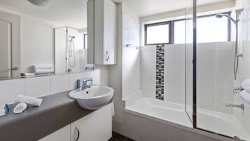 Un baño moderno con ducha de vidrio, bañera y un espejo grande sobre el lavamanos.