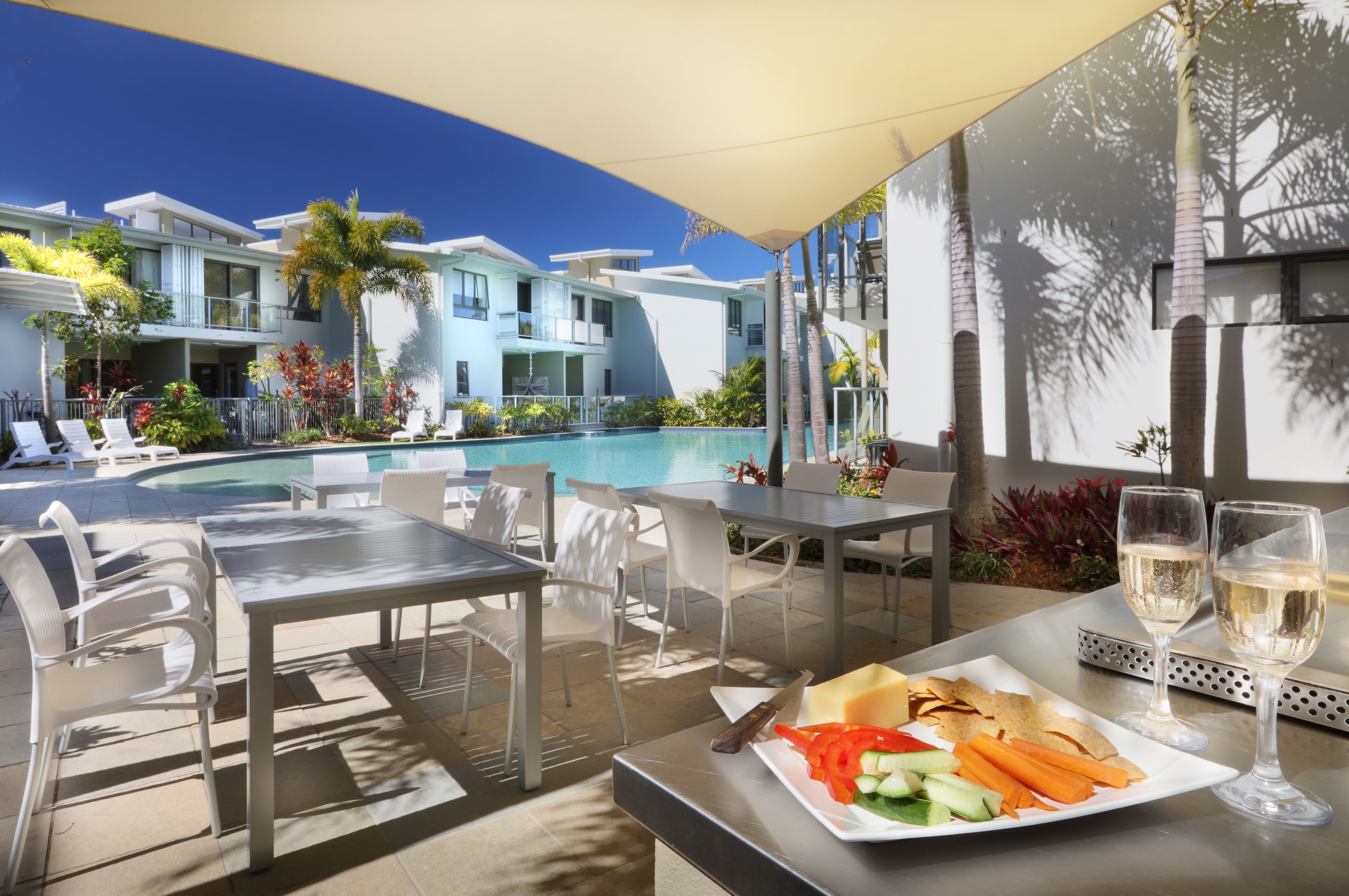 Área de refeições junto à piscina, com mesa, cadeiras e um prato de comida.