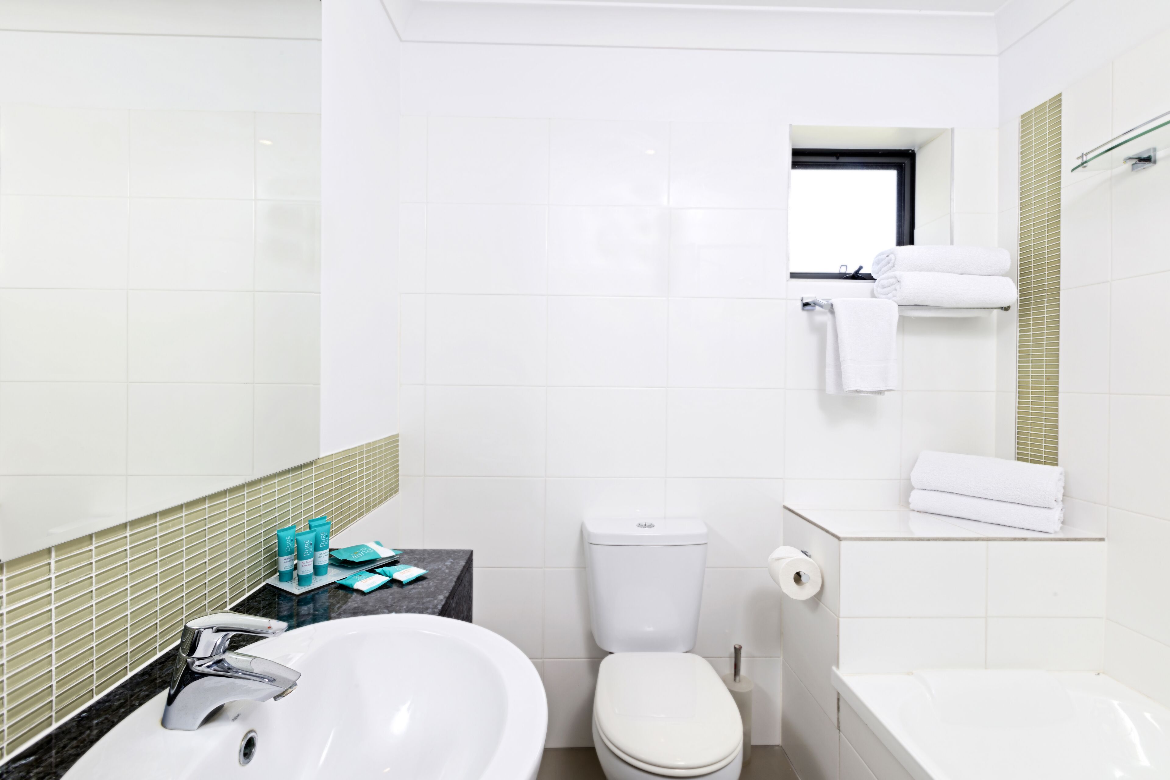 A modern bathroom with a white sink, toilet, and bathtub. There is a small countertop with toiletries and a mirror above the sink.