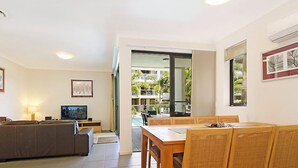 Una sala de estar moderna con sofá, televisor y zona de comedor con sillas.