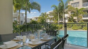 Un comedor con una mesa dispuesta para cuatro personas, con vista a una piscina y palmeras.