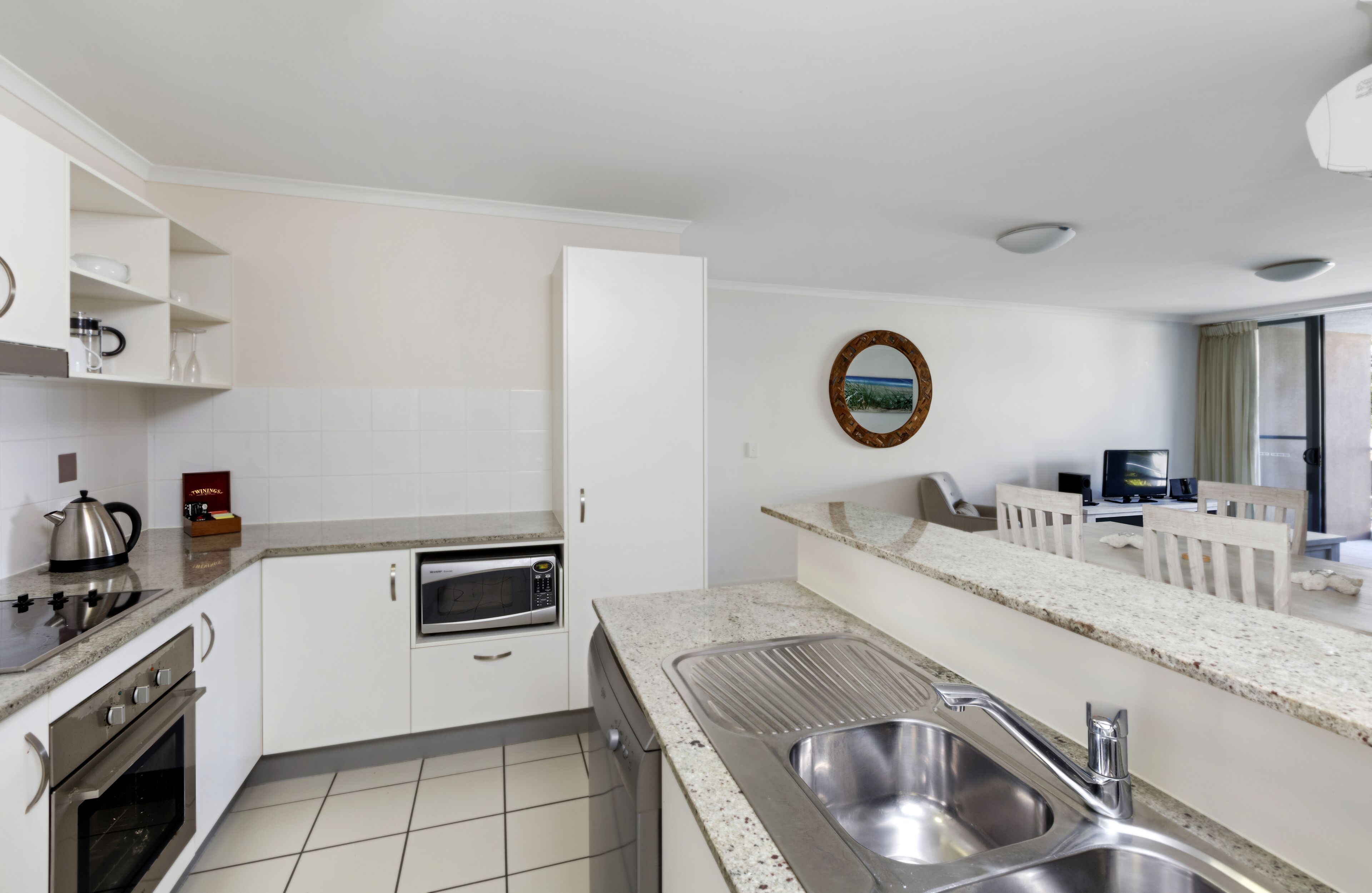 A modern kitchen with white cabinetry, a stainless steel sink, a microwave, and a stove.