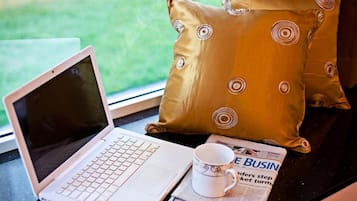 A laptop on a glass table with a newspaper and a cup beside it.
