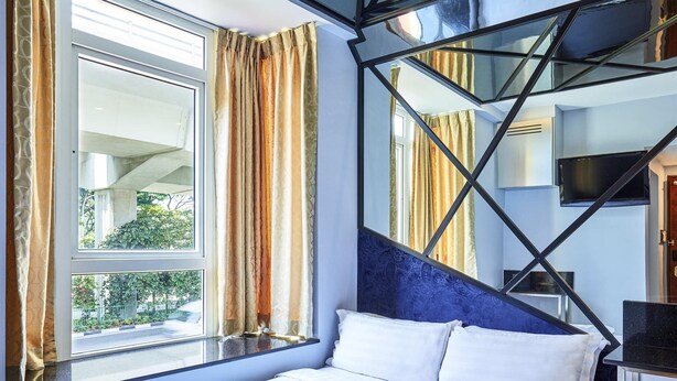 Habitación de hotel con cama, ventana con cortinas, televisor montado en la pared y un diseño de techo geométrico único.