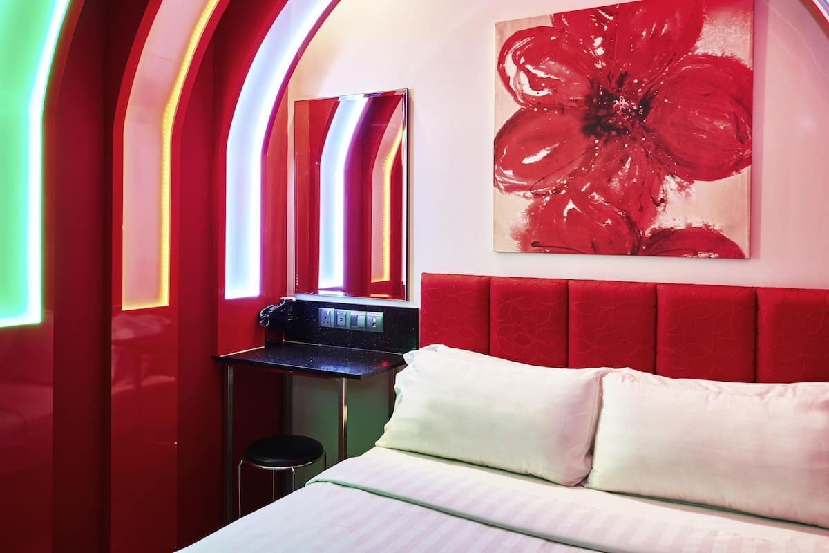 A hotel room with a bed, a desk, and a large red floral painting on the wall.