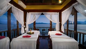 Een kamer met twee bedden, een tafel en uitzicht op zee.
