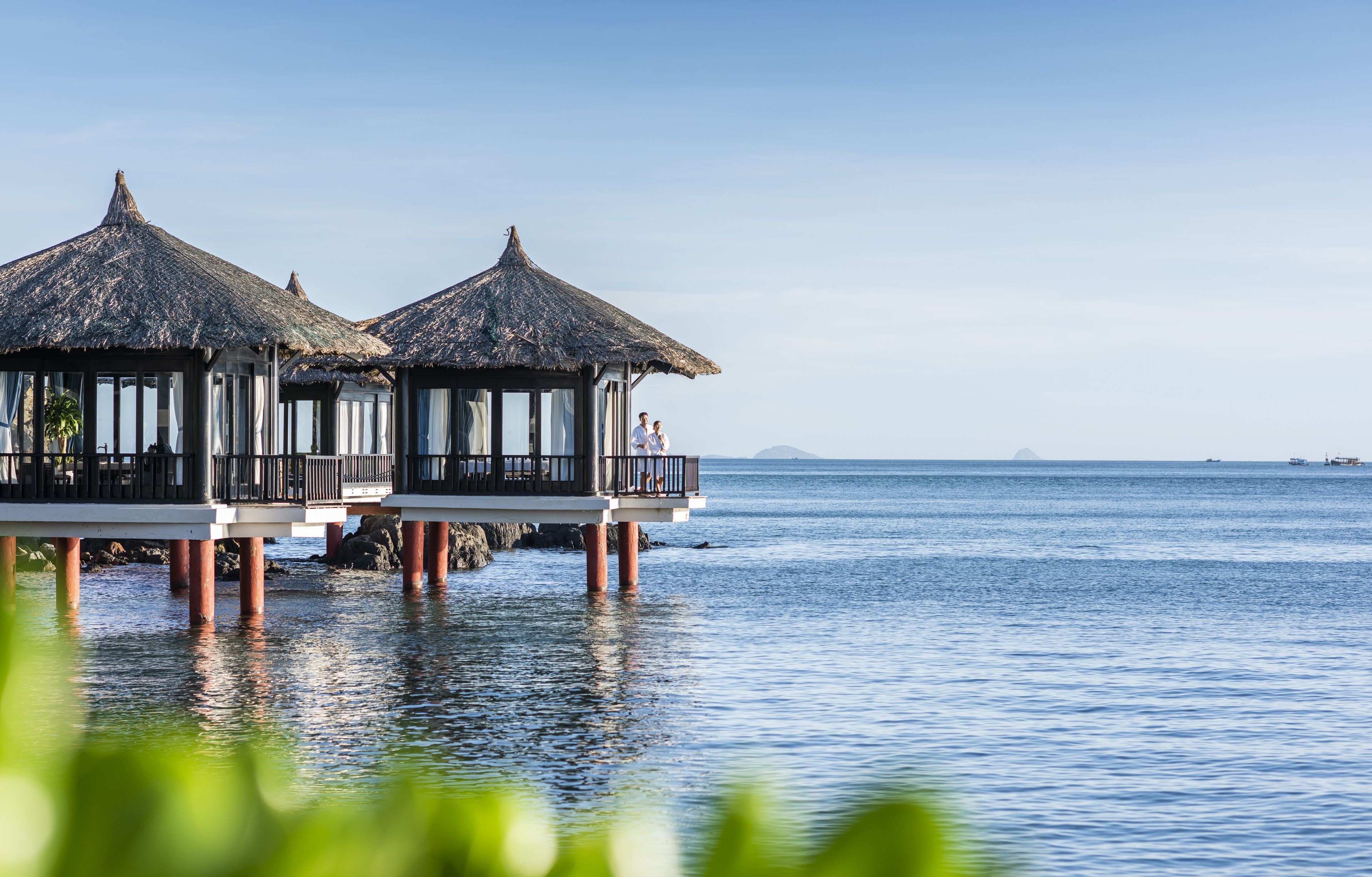 Overwater bungalows with thatched roofs, built on stilts over calm sea water.