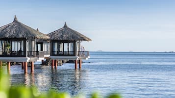 Overwater bungalows with thatched roofs, built on stilts over calm sea water.