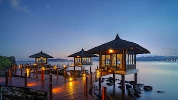 A wooden deck with thatched-roof structures, overlooking calm water.