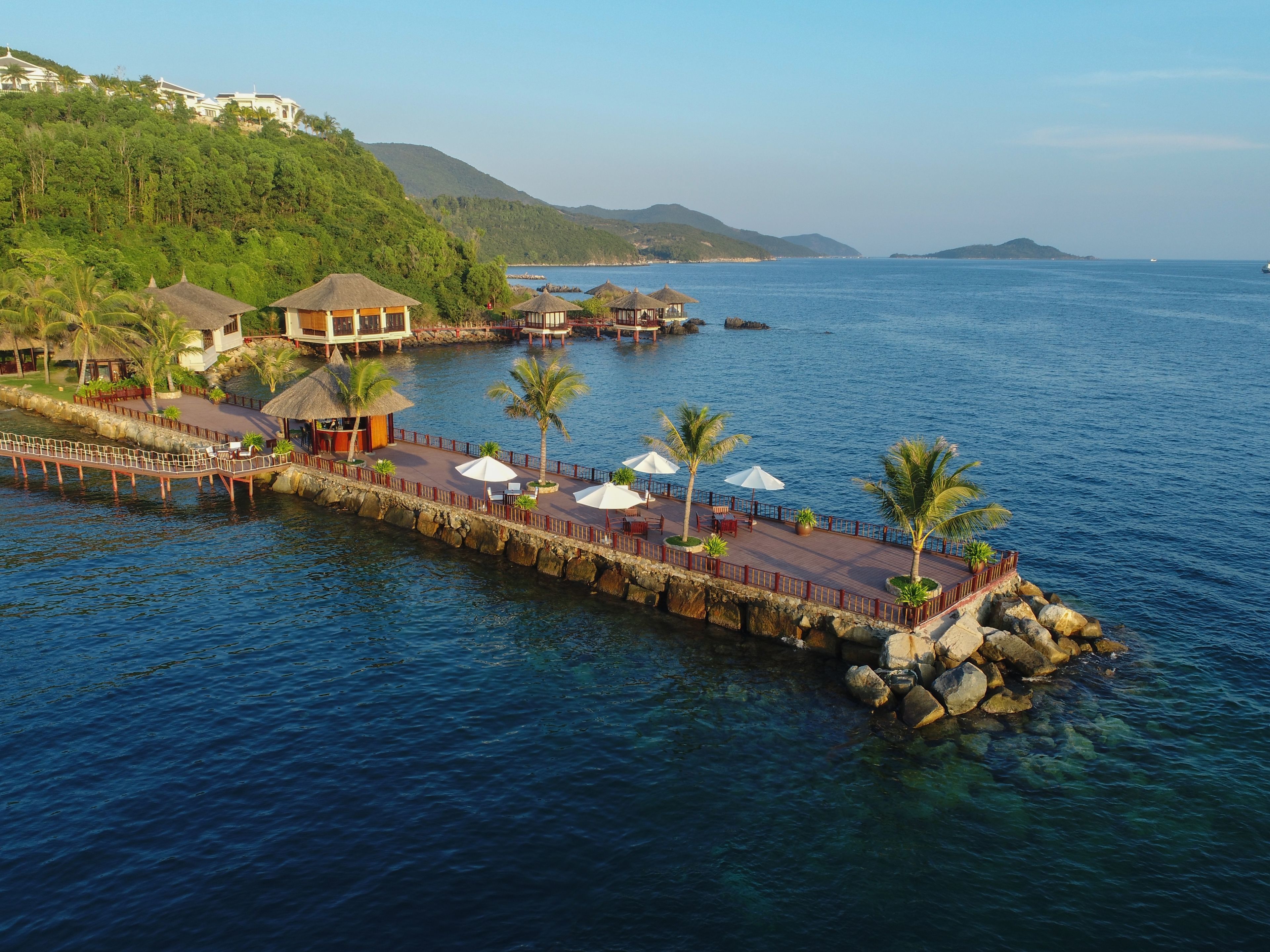 A coastal resort with a pier extending into the water, featuring thatched-roof structures and outdoor seating areas.