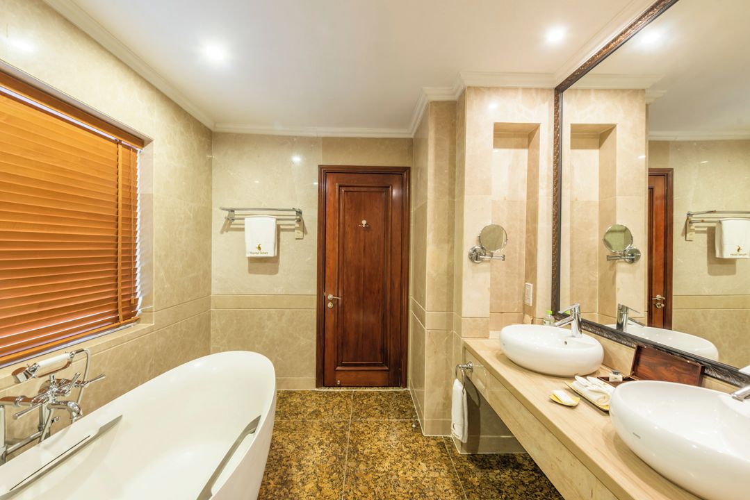 A hotel bathroom with a bathtub, two sinks, a large mirror, and a door.