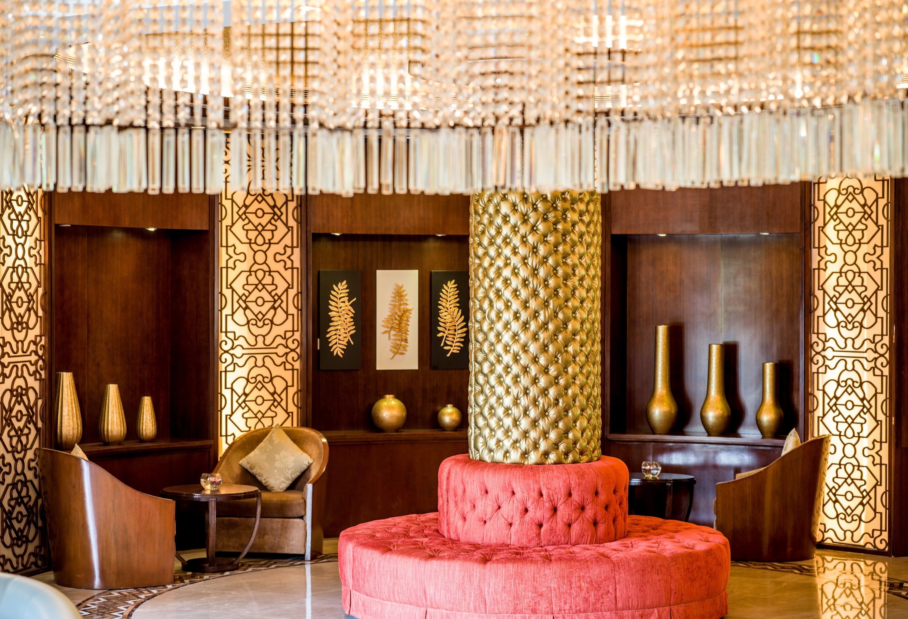Un vestíbulo lujoso con un sofá capitonado rojo, jarrones decorativos y diseños complejos en las paredes.