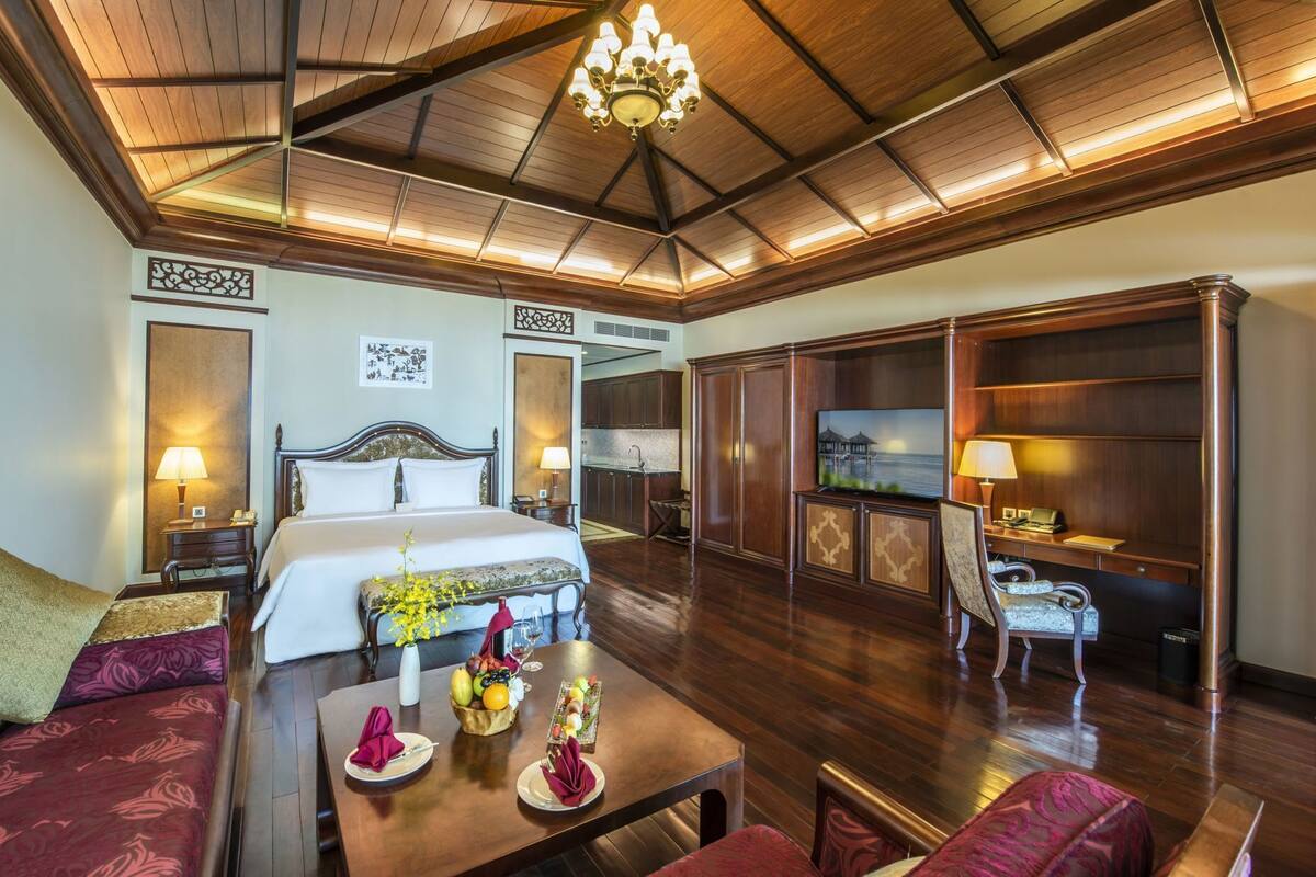 Een hotelkamer met een bed, een eettafel met fruit, een televisie en uitzicht op zee.