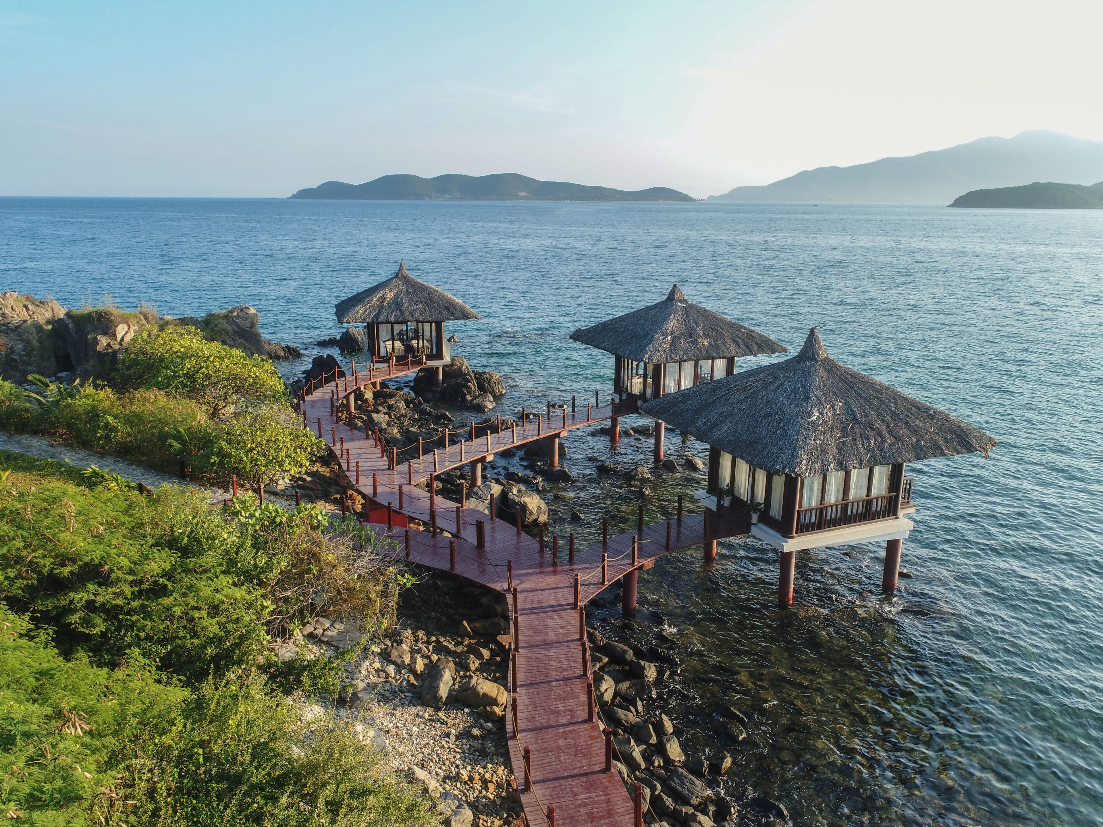 A wooden deck leading to overwater bungalows with thatched roofs.