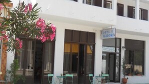 Hotelli nimeltä ”HOTEL ISIDORA”, jossa on valkoinen julkisivu, suuret ikkunat ja ulkona oleva oleskelualue, jossa on vihreitä tuoleja.