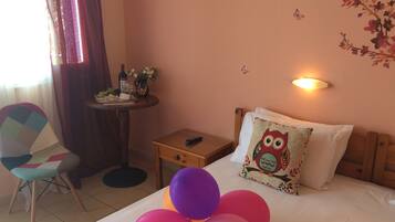 Hotelkamer met een bed, een tafeltje met een fles en bloemen, een stoel en een muur met een vlinderstickersetting.