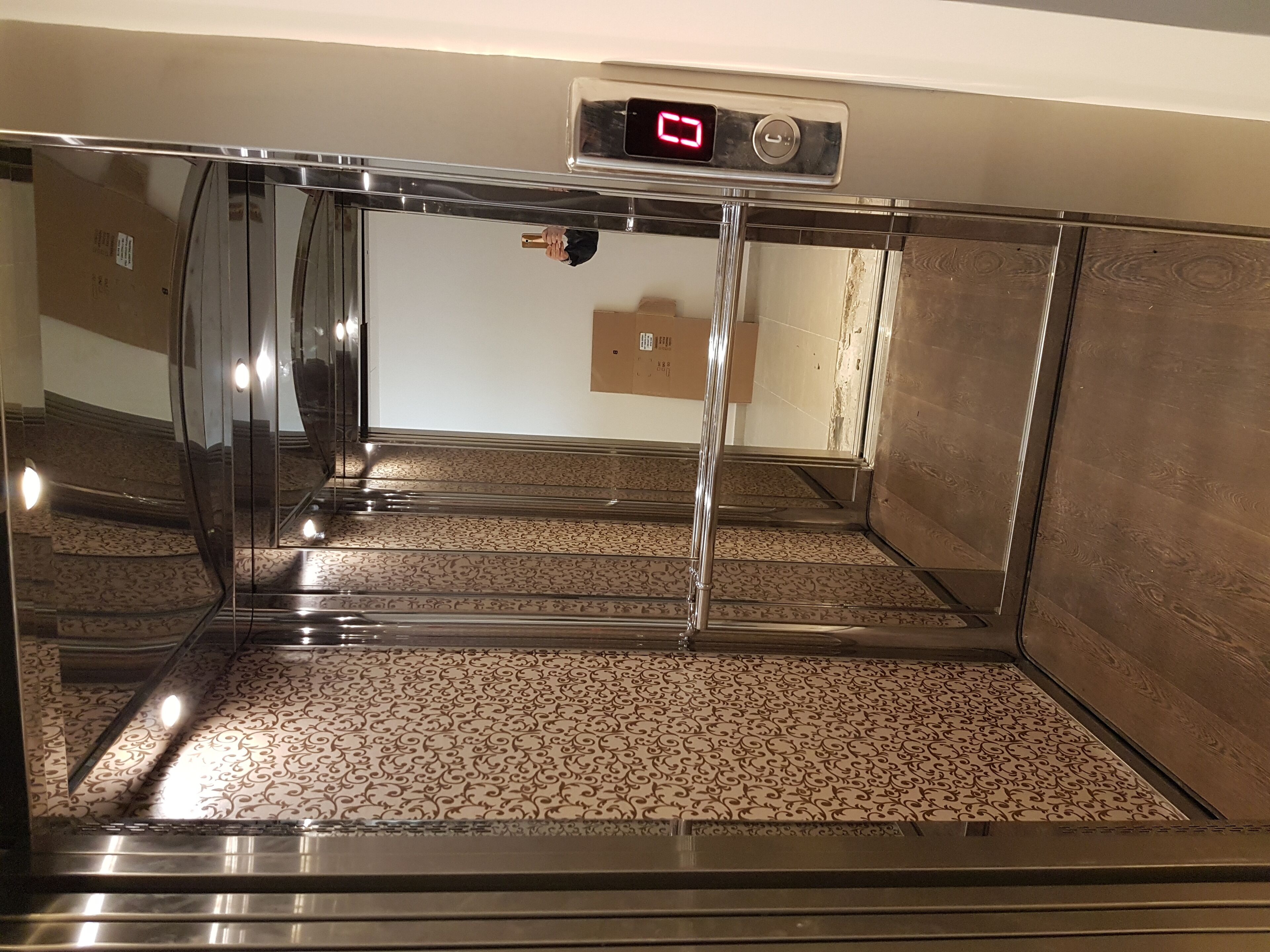 An elevator with a digital display, patterned floor, and metallic walls.