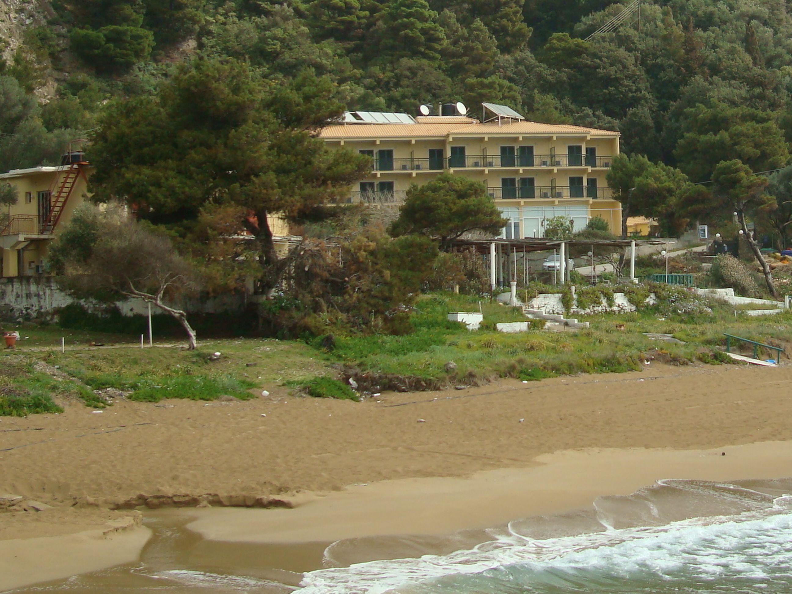 A coastal building with multiple balconies, surrounded by greenery and a sandy beach.
