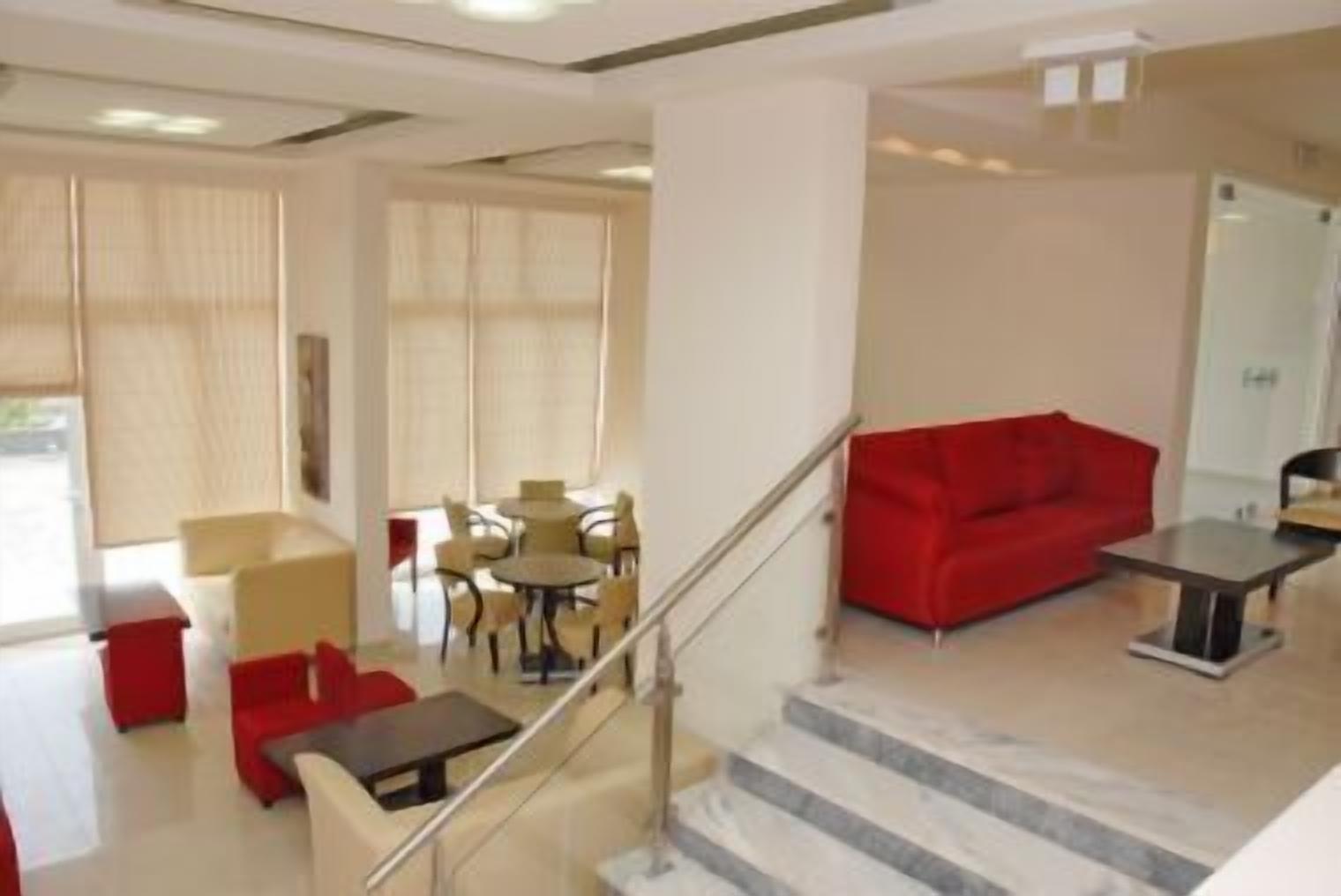 A modern hotel lobby with a staircase, a red sofa, a round table, and a seating area with chairs.