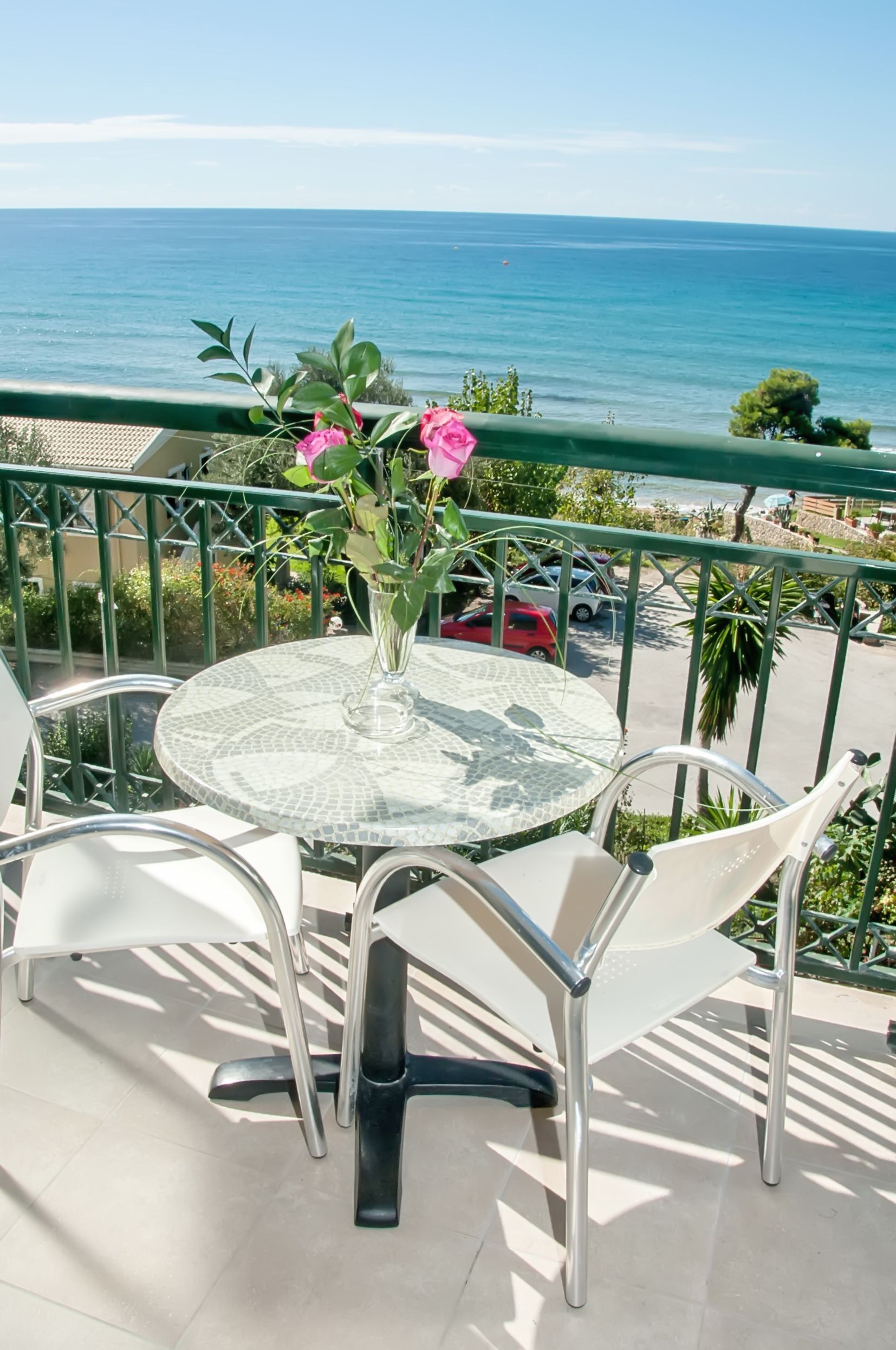 Una mesa de vidrio redonda con un florero de flores rosas, dos sillas blancas y vistas al mar.